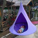 Floating Teepee Chair hammock With small child laying inside hanging from a tree in a small village