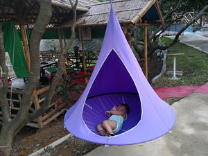 Floating Teepee Chair hammock With small child laying inside hanging from a tree in a small village