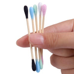 Double sided Bamboo Q-tips blue, green, white pink, and black held in the finger tips of a hand