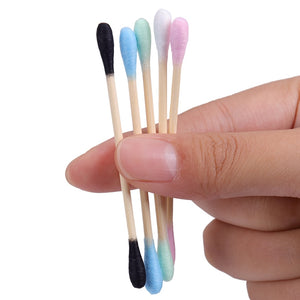 Double sided Bamboo Q-tips blue, green, white pink, and black held in the finger tips of a hand