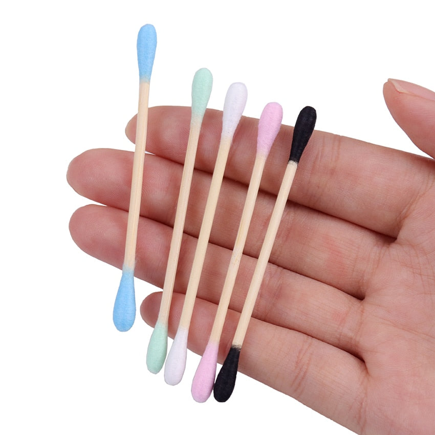 Double sided Bamboo Q-tips blue, green, white pink, and black held in a hand