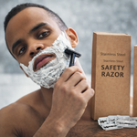 Man shaving with a safety razor next to two boxes of stainless steel safety razors.