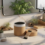Brown cylindrical container with black cotton swabs on a white background